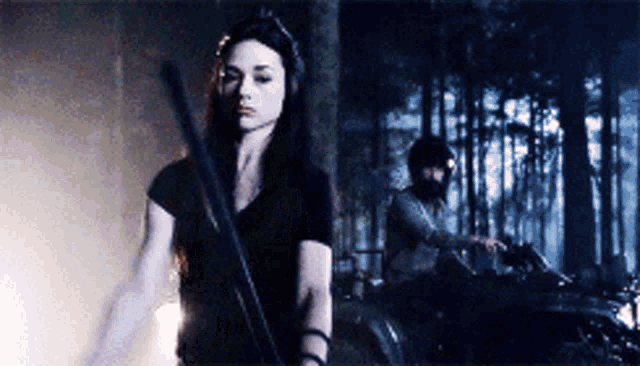 a woman is holding a sword while a man is riding a motorcycle in the background
