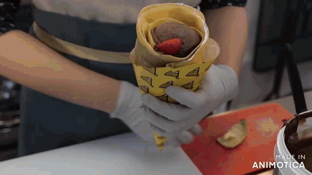 a person is holding a crepe with a strawberry on top and the words made in animotica in the corner