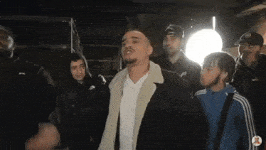 a group of men are standing in a dark room and one of them is wearing a jacket with a fur collar .