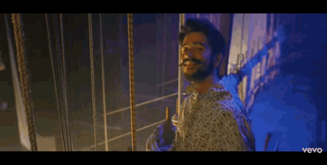 a man with a beard is standing in a dark room with a rope around his neck .