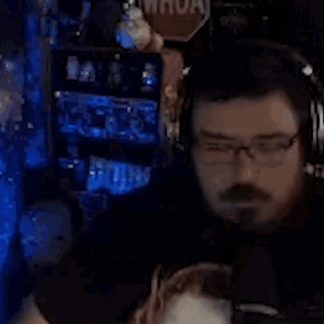 a man with glasses and a beard is sitting in front of a microphone .