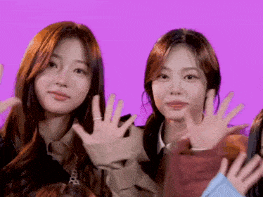 two girls are waving their hands in front of a pink background .
