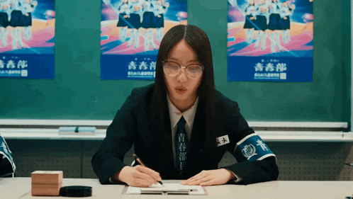 a girl wearing glasses sits at a desk in front of a poster that says ' youth club ' on it