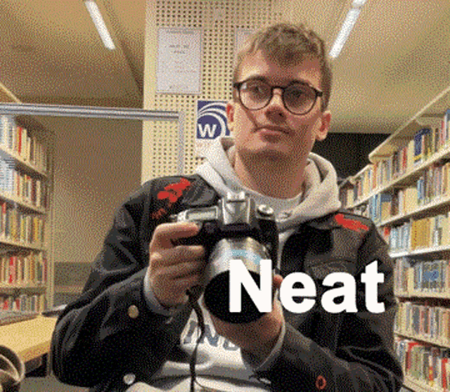 a young man is holding a camera in a library and the word neat is on the bottom