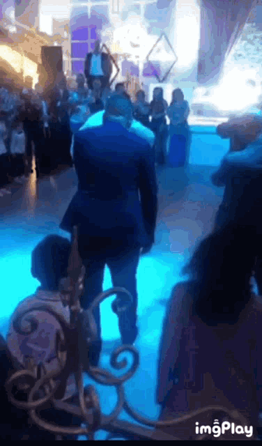 a man in a suit stands in front of a crowd of people in a room with blue lights