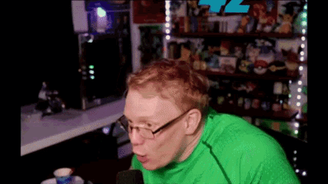 a man wearing glasses and a green shirt is sitting in front of a microphone in a room .