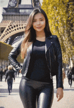 a woman wearing a black leather jacket and pants stands in front of the eiffel tower