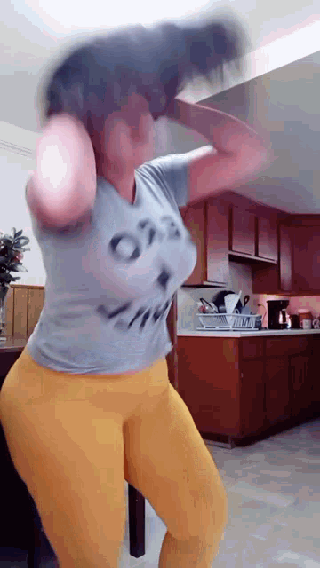 a woman is dancing in a kitchen wearing a grey shirt that says ots