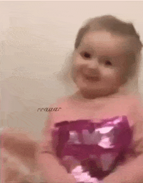 a baby girl in a pink dress is smiling and looking at the camera .