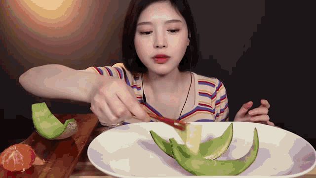 a woman in a striped shirt is eating a plate of fruit
