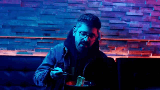 a man is sitting at a table eating noodles with chopsticks in a restaurant .