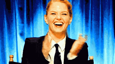 a woman in a suit and tie is smiling and clapping her hands