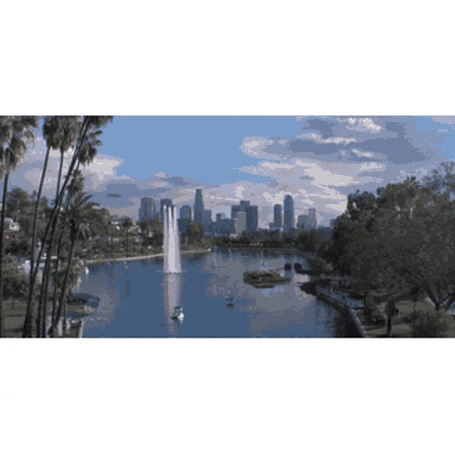 a lake with a fountain in the middle and the city skyline in the background