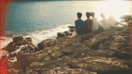 a group of people are sitting on rocks near the ocean looking at the water .