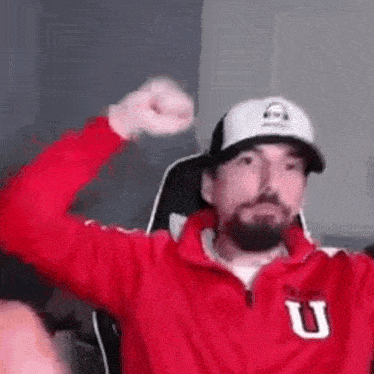 a man with a beard wearing a red jacket and a white hat is sitting in a chair .