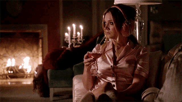 a woman is sitting in front of a fireplace holding a wine glass