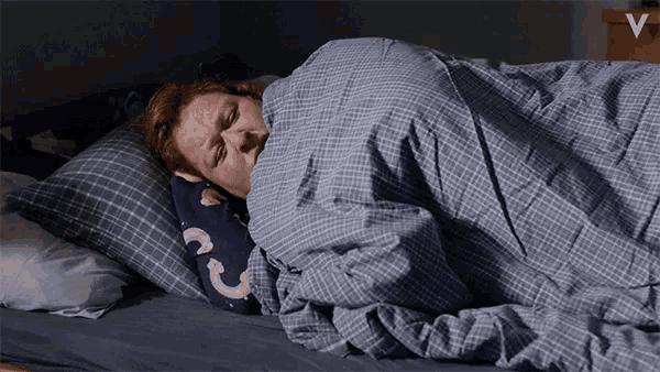a person laying in bed with a blue plaid blanket and a pillow with the letter c on it