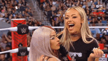 two women are laughing in a wrestling ring with a crowd watching .