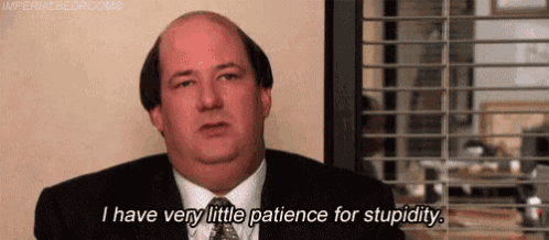 a bald man in a suit and tie is sitting in front of a window and talking .