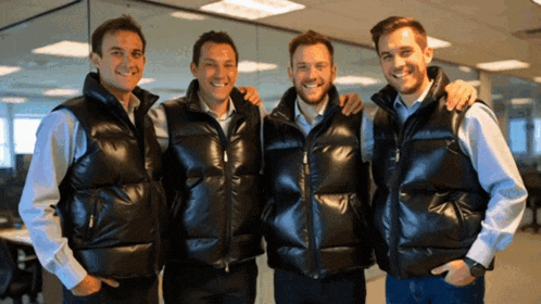 four men wearing black vests are posing for a picture together