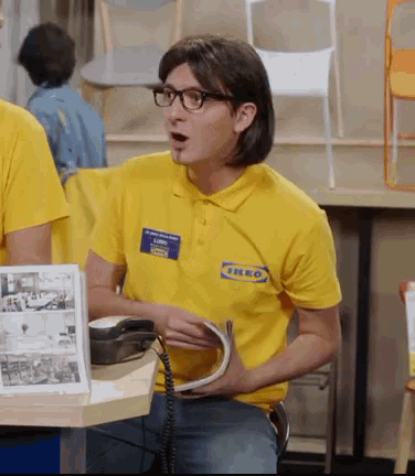 a man wearing a yellow ikea shirt holds a phone