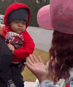 a woman is holding a baby in her arms and the baby is wearing a spiderman hoodie .