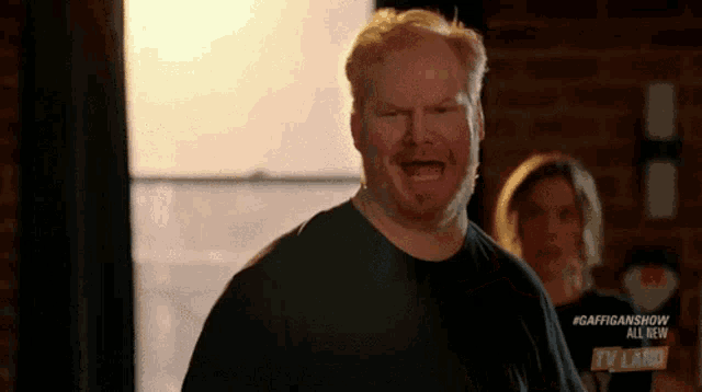 a man with a beard is making a funny face in front of a brick wall .