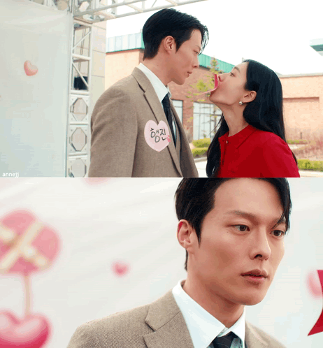 a man in a suit kisses a woman on the cheek while wearing a heart shaped badge