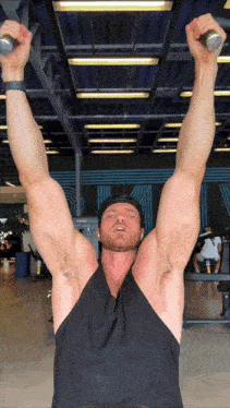 a man in a black tank top holds a barbell over his head