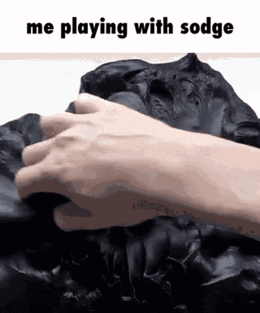 a person 's hand is playing with a black substance .