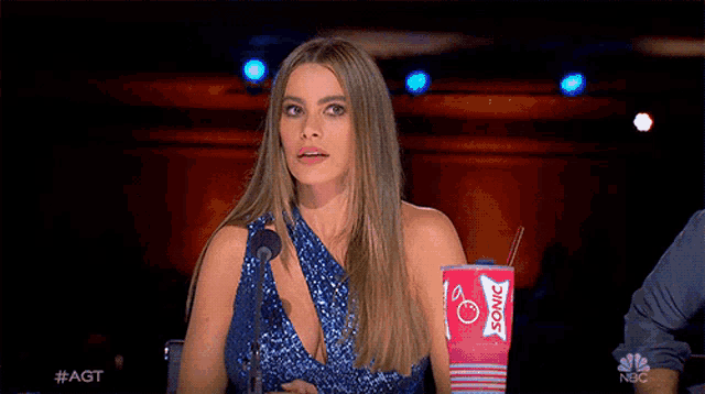 a woman in a blue dress is holding a sonic drink