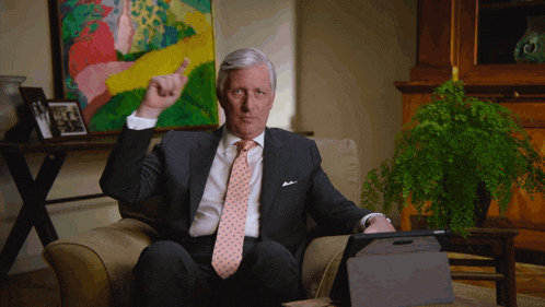 a man in a suit and tie is sitting in a chair and pointing up