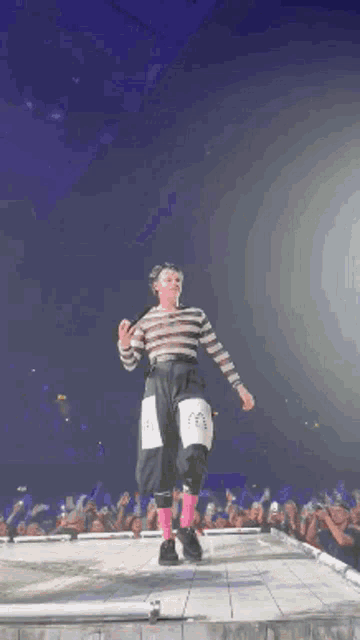 a man in a striped shirt and pink socks is dancing on a stage in front of a crowd