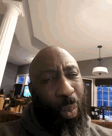 a bald man with a beard is looking at the camera in a living room