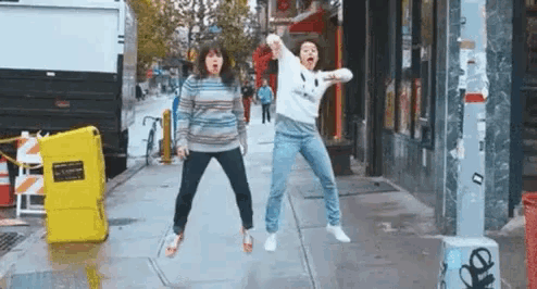 two women are jumping in the air on a sidewalk in front of a building .