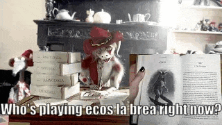 a stuffed animal is sitting at a table with a stack of books and a person is holding a book .