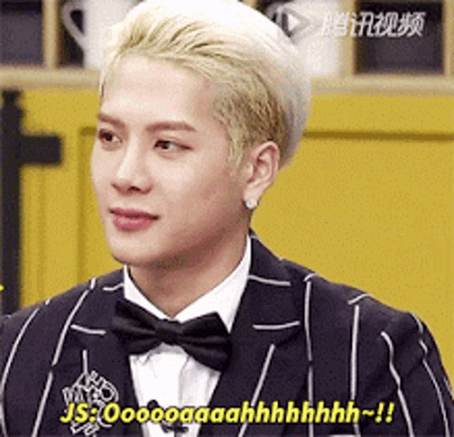 a man with blonde hair is wearing a suit and bow tie and is talking .