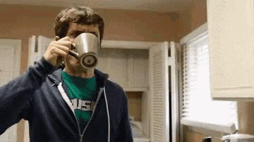 a man is drinking from a mug in a kitchen while wearing a green shirt that says usc