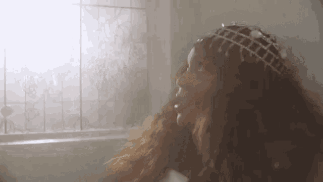 a woman with long hair is wearing a tiara and looking out a window .