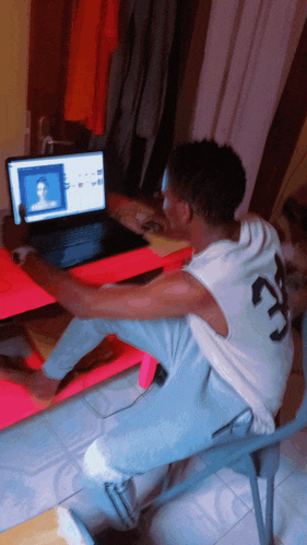 a man wearing a white shirt with the number 23 on it sits in front of a laptop