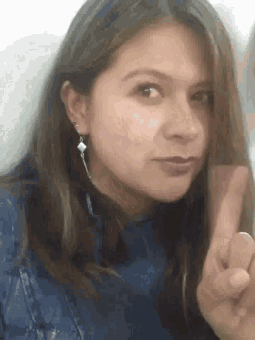 a woman wearing earrings is making a peace sign with her finger