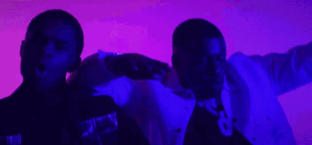 a couple of men are standing next to each other in front of a purple background in a dark room .