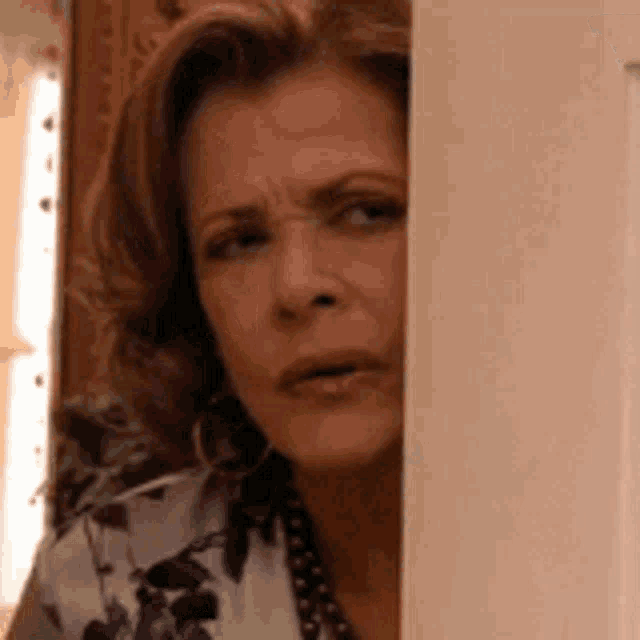 a woman is peeking out from behind a wall and making a face .