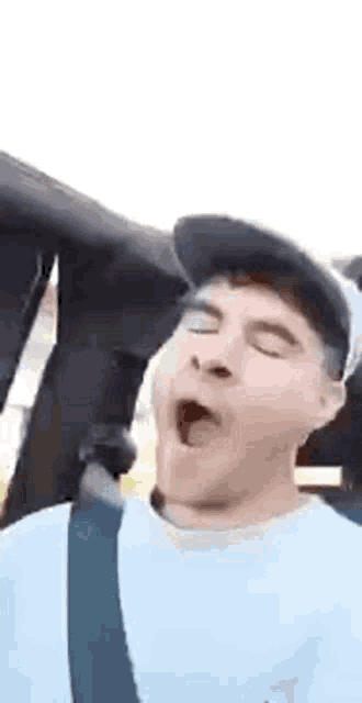a man in a baseball cap is yawning in a car .