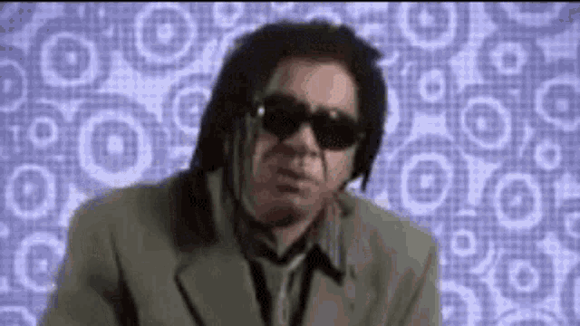 a man with dreadlocks is wearing sunglasses and a suit and tie .