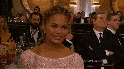 a woman in a pink dress is sitting in a crowd of people at a golden globes awards ceremony .