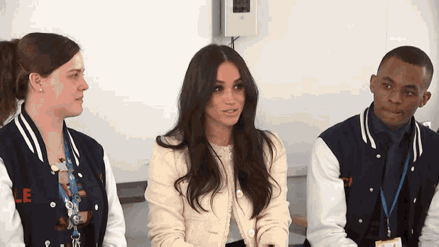 a woman in a white jacket sits next to a man and a woman in varsity jackets