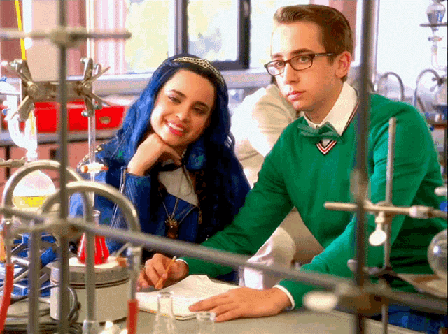 a boy in a green sweater sits next to a girl with blue hair in a lab