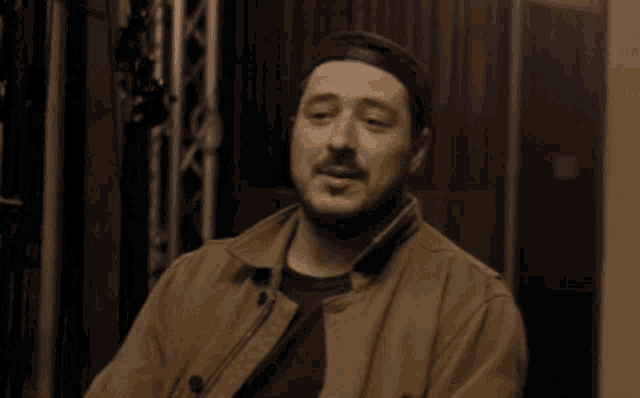 a man with a beard is wearing a hat and a brown jacket