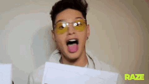 a man wearing yellow sunglasses is sticking his tongue out while holding a piece of paper .